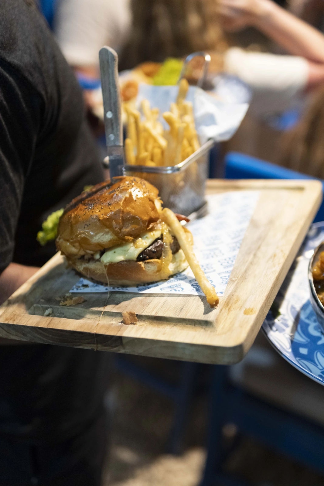 Hamburguesa gourmet con papas fritas en tabla de madera en Cocos Beach Front
